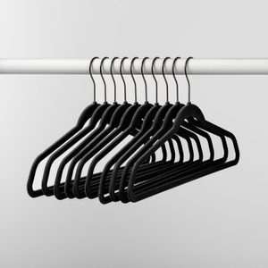 Black hangers are hanging from a white rod, aligned neatly, in a minimalist setting.