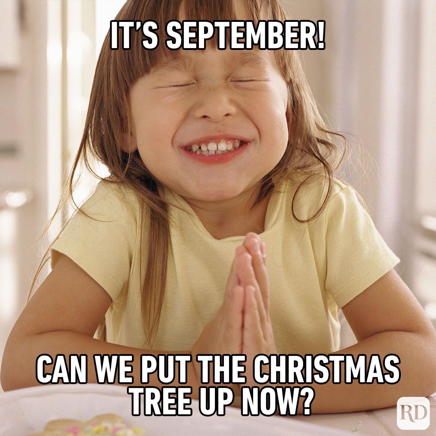Child grinning with clasped hands, sitting indoors. Text: "IT'S SEPTEMBER! CAN WE PUT THE CHRISTMAS TREE UP NOW?"