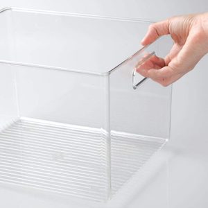 Hand holding a clear plastic storage bin by its handle, set against a plain, light background.