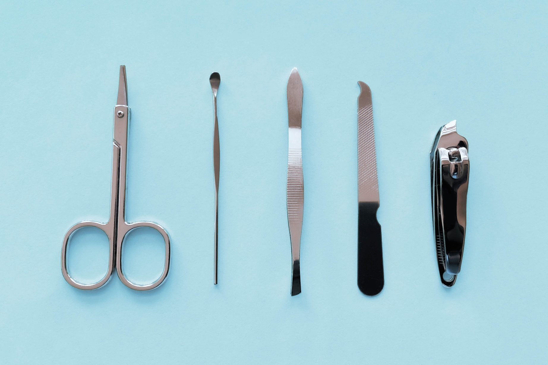 Travel-size manicure tools (scissors, cuticle pusher, tweezers, nail file and nail clippers) on soft blue background