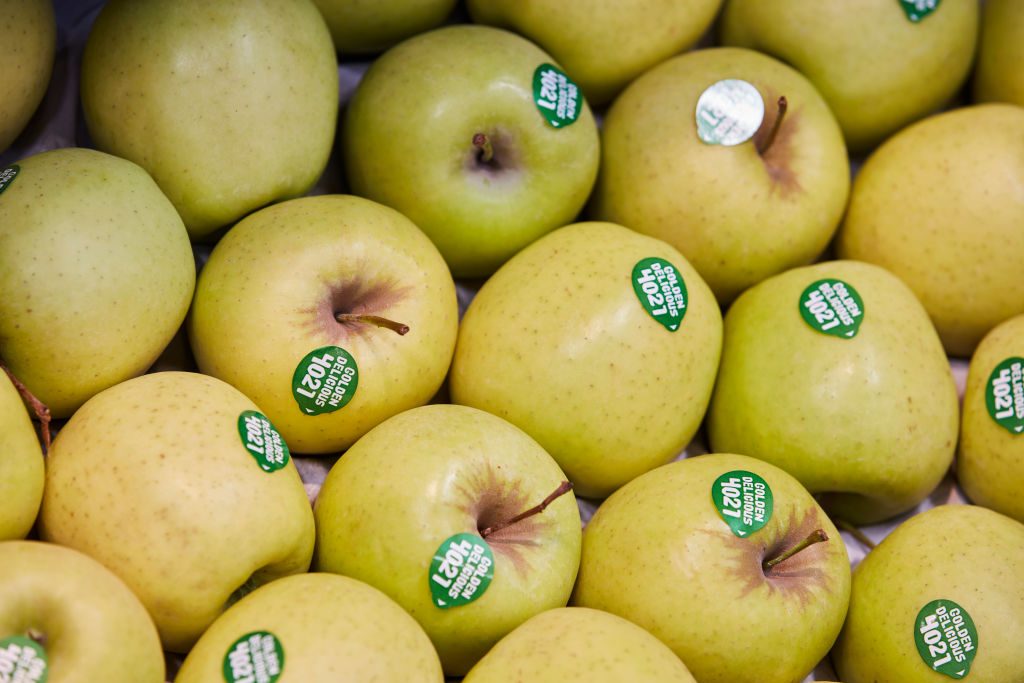Apples rest closely together, each displaying a green sticker reading "Golden Delicious 4021" in a market setting.