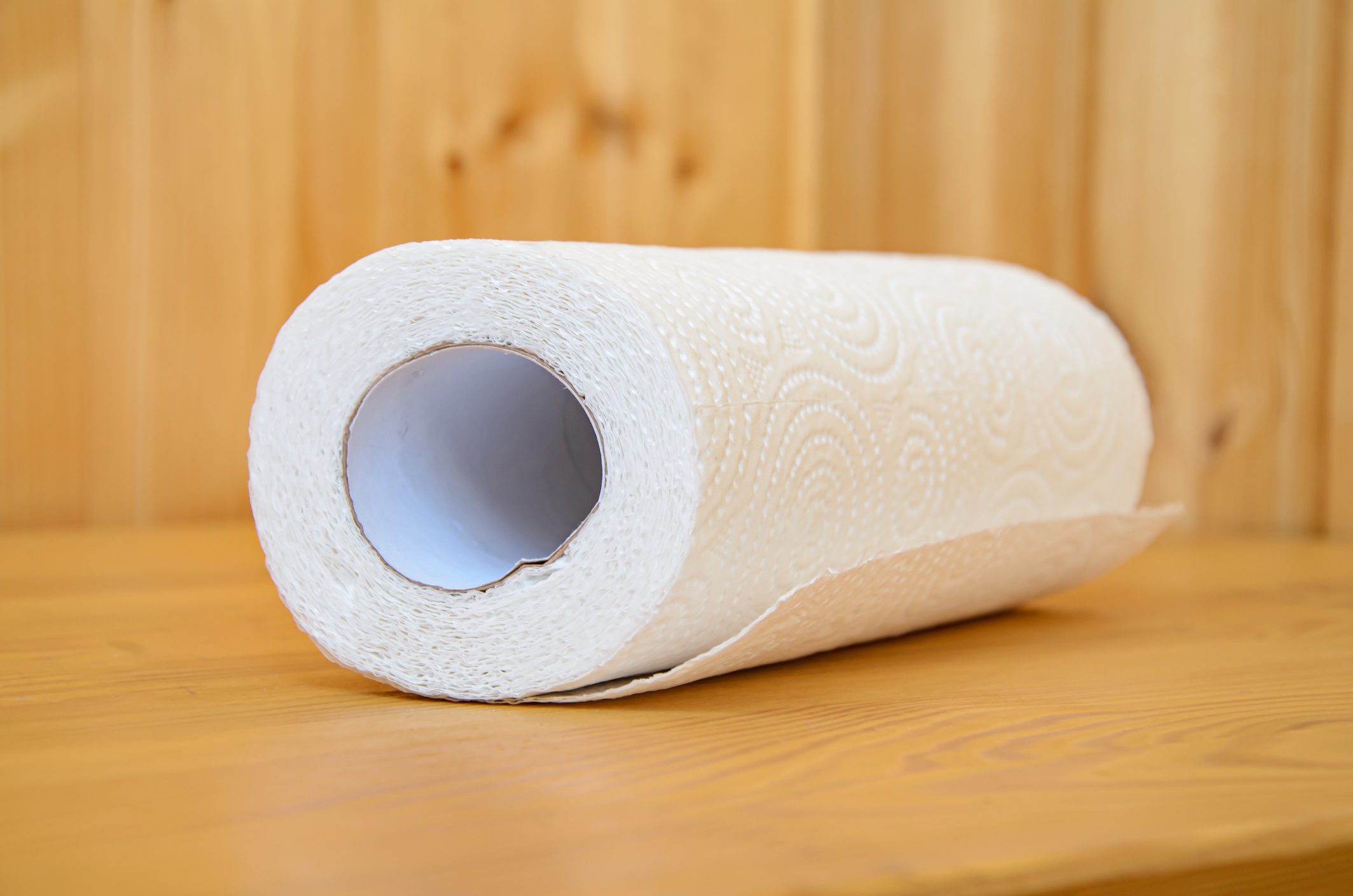 A roll of paper towels rests on a wooden table, displaying embossed patterns on the sheets.