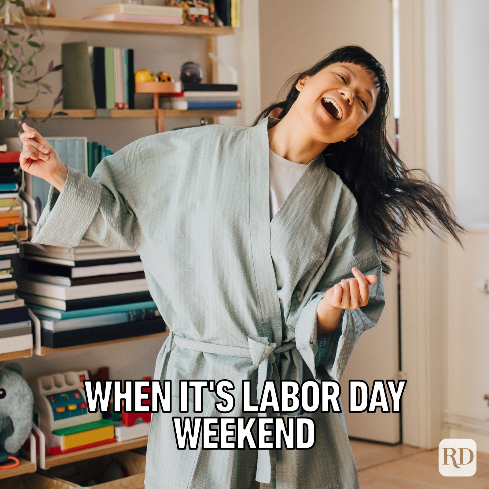 Person joyfully dancing in a robe, surrounded by a room full of books and shelves. Text reads, "WHEN IT'S LABOR DAY WEEKEND."