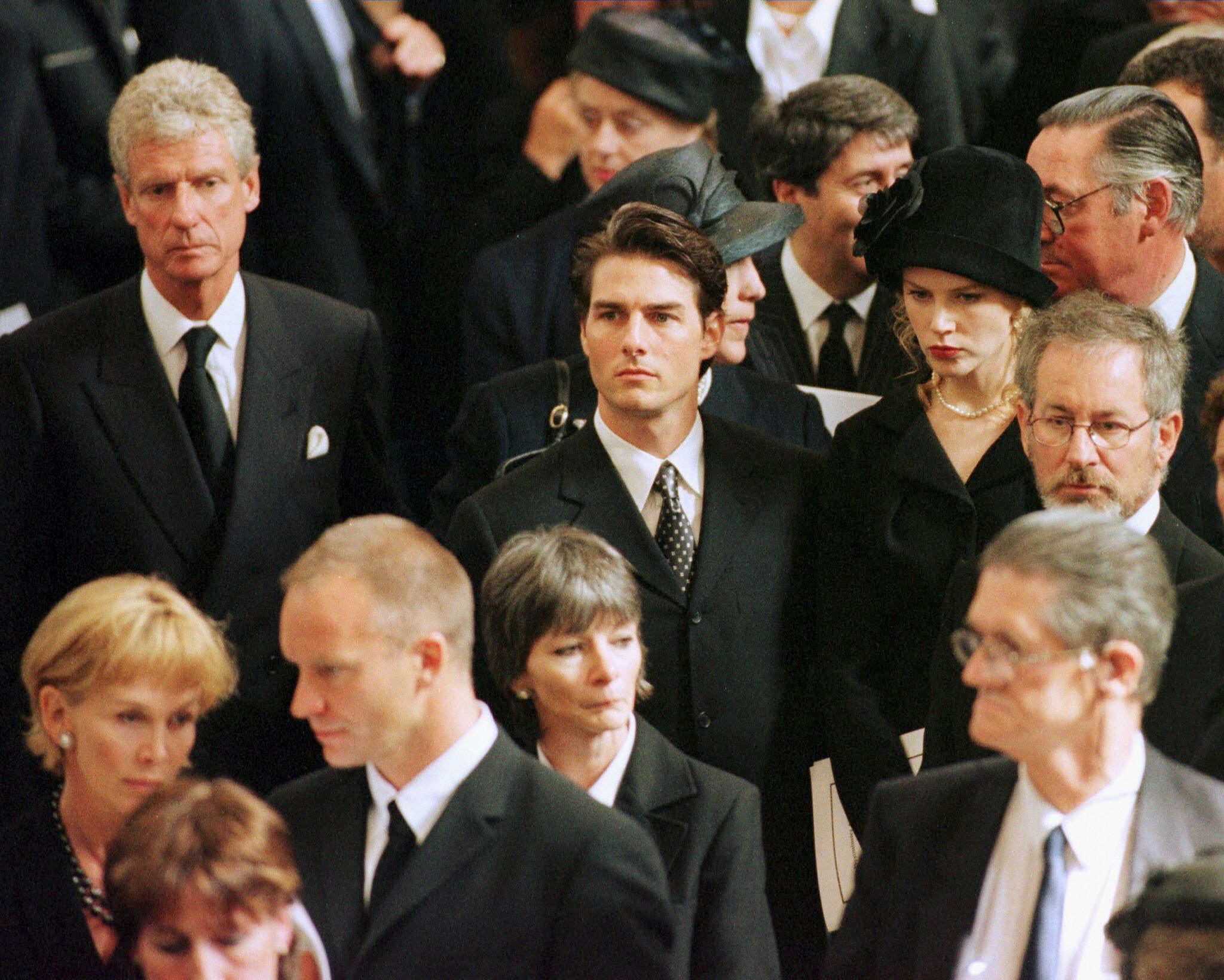 A group of solemnly dressed people stands closely together, attentively focused, likely at a formal event or ceremony.