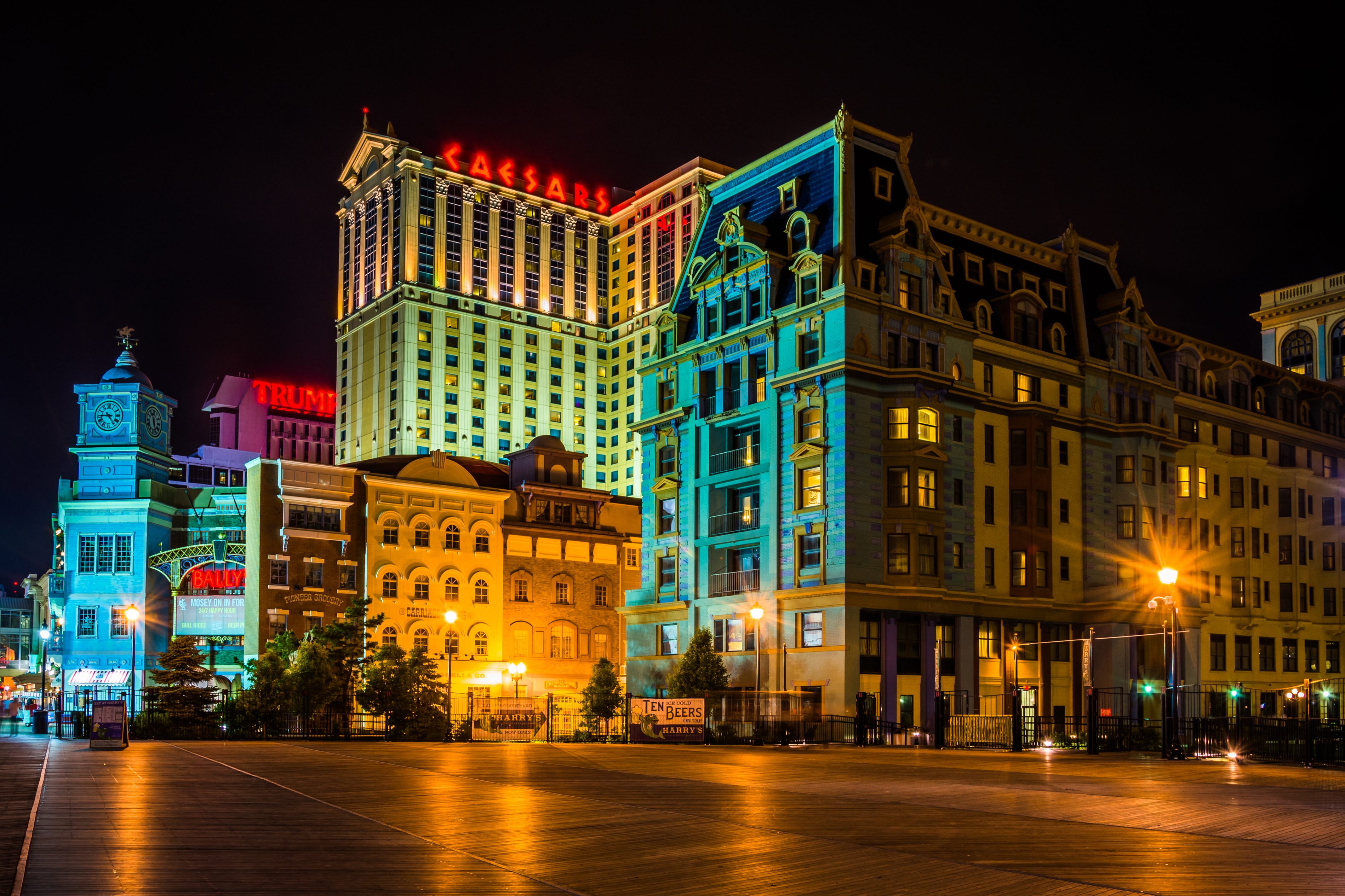 Buildings illuminated at night, featuring bright signs including "Caesars," "Trump," and "Bally's." The scene is set on an empty boardwalk.