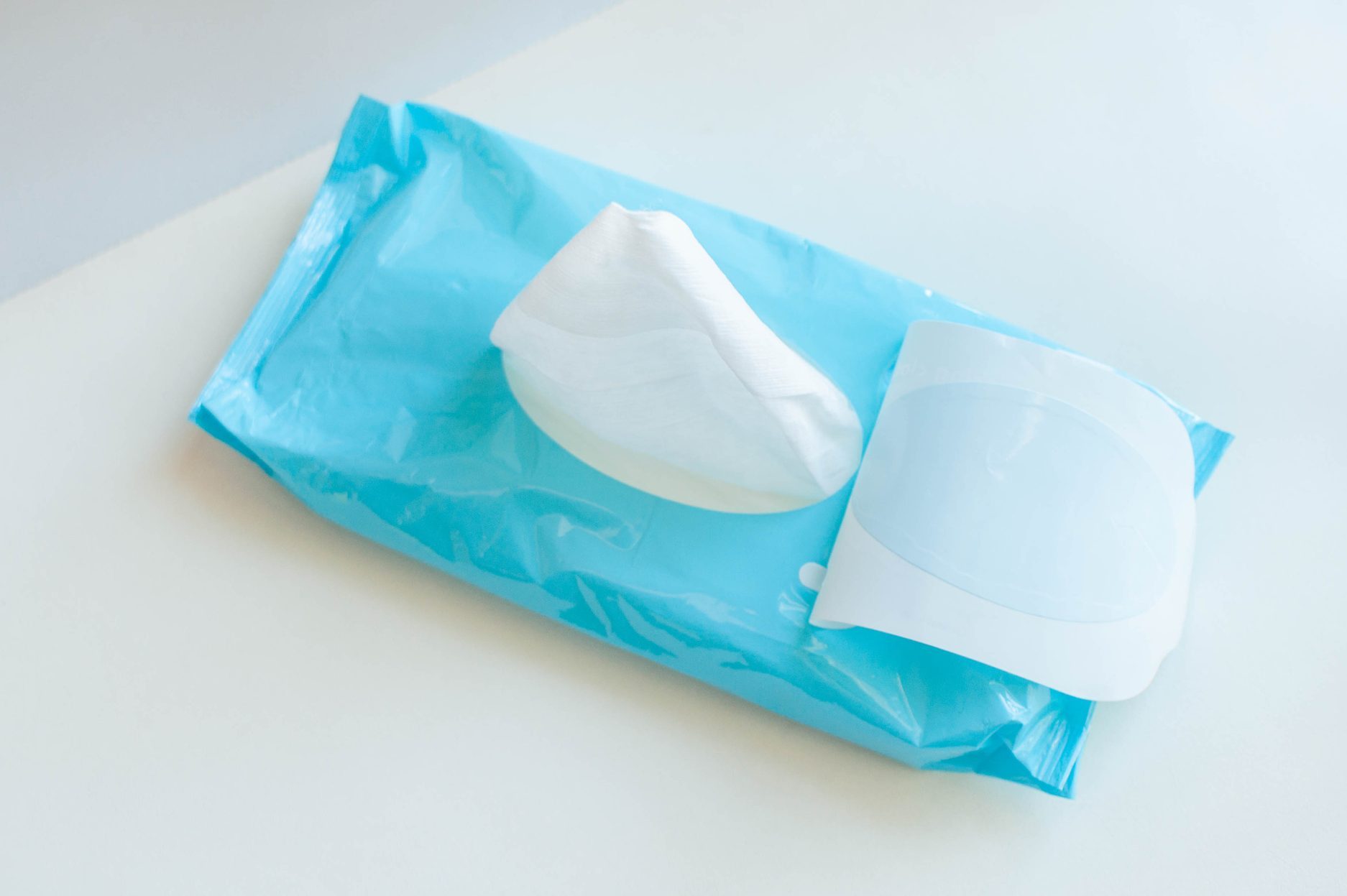 A pack of baby wipes with one wipe pulled out, resting on a white surface.