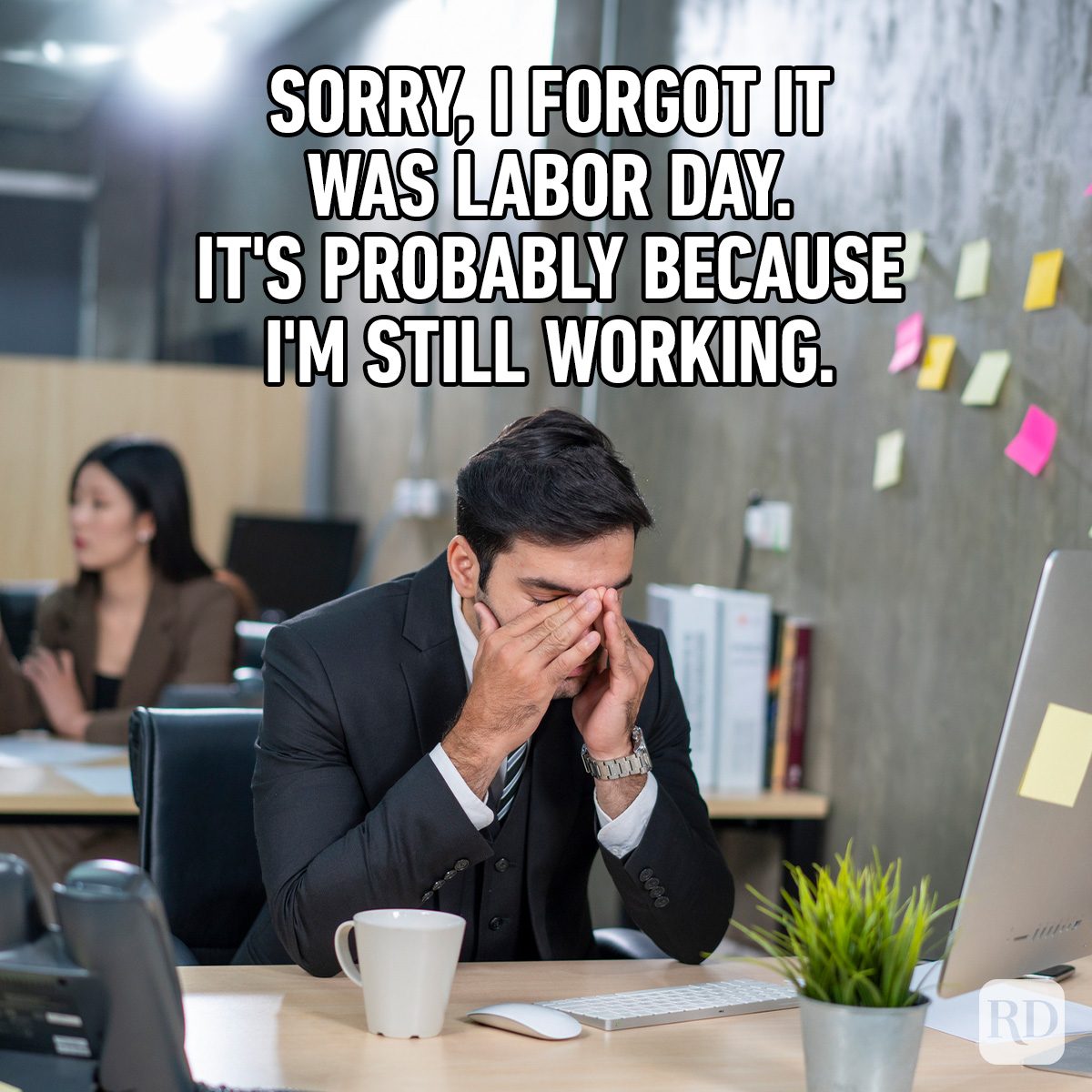 Man covers face at desk, looking stressed. Office setting with computers and sticky notes. Text reads: "Sorry, I forgot it was Labor Day..."