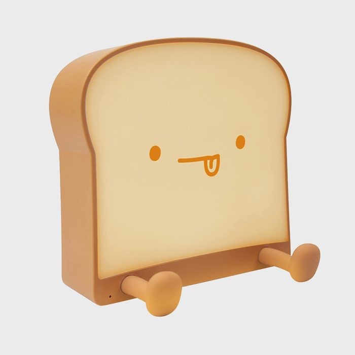 A toast-shaped lamp glows softly, featuring a cute face with eyes and a tongue, set against a plain background.
