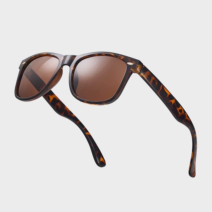 Tortoiseshell sunglasses with brown lenses rest suspended against a plain, light gray background.