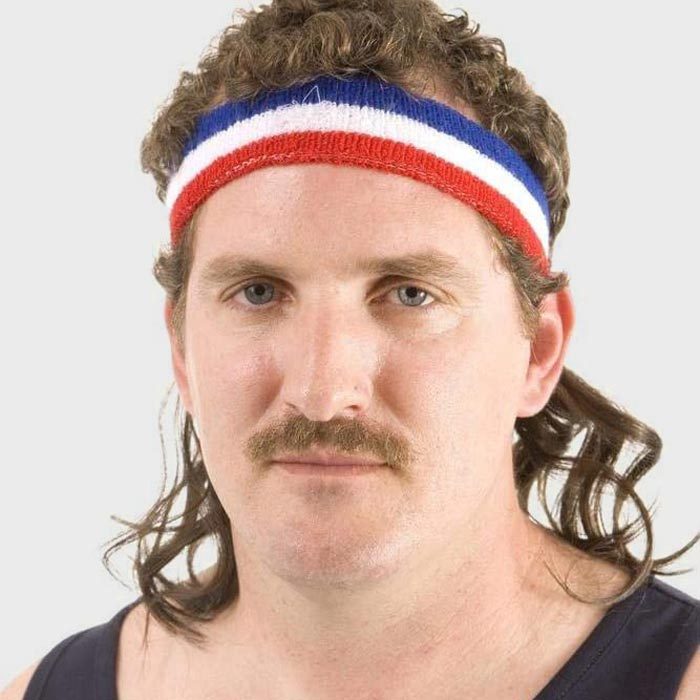 Man staring forward, wearing a red, white, and blue headband with a mullet hairstyle, against a plain background.