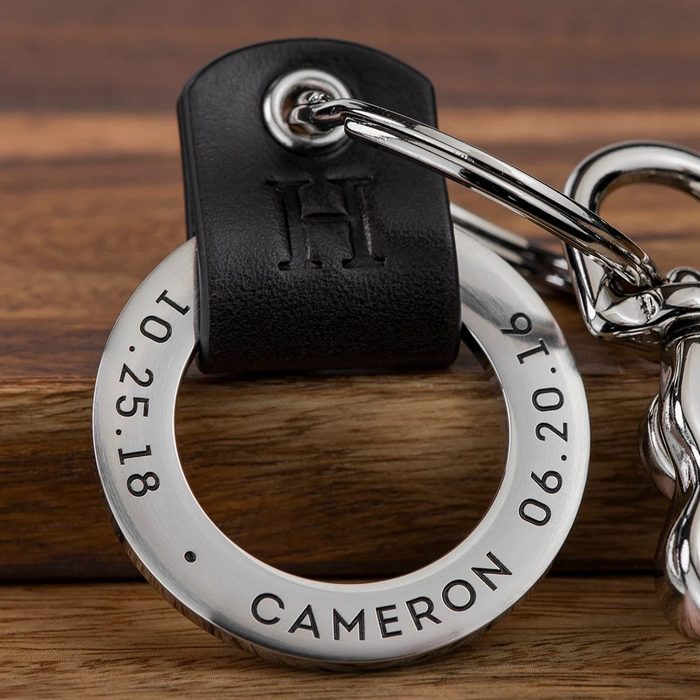 Metal keyring rests on wood, featuring engraved dates and the name 