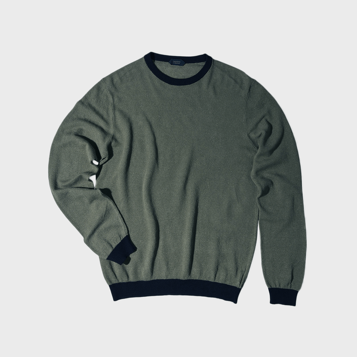 A green sweater with dark trim lies flat against a plain, light background.
