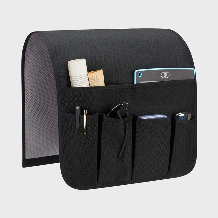 Organizer hangs over furniture edge, holding various items like books, pens, gadgets, and glasses. Black with multiple pockets, used in home or office.