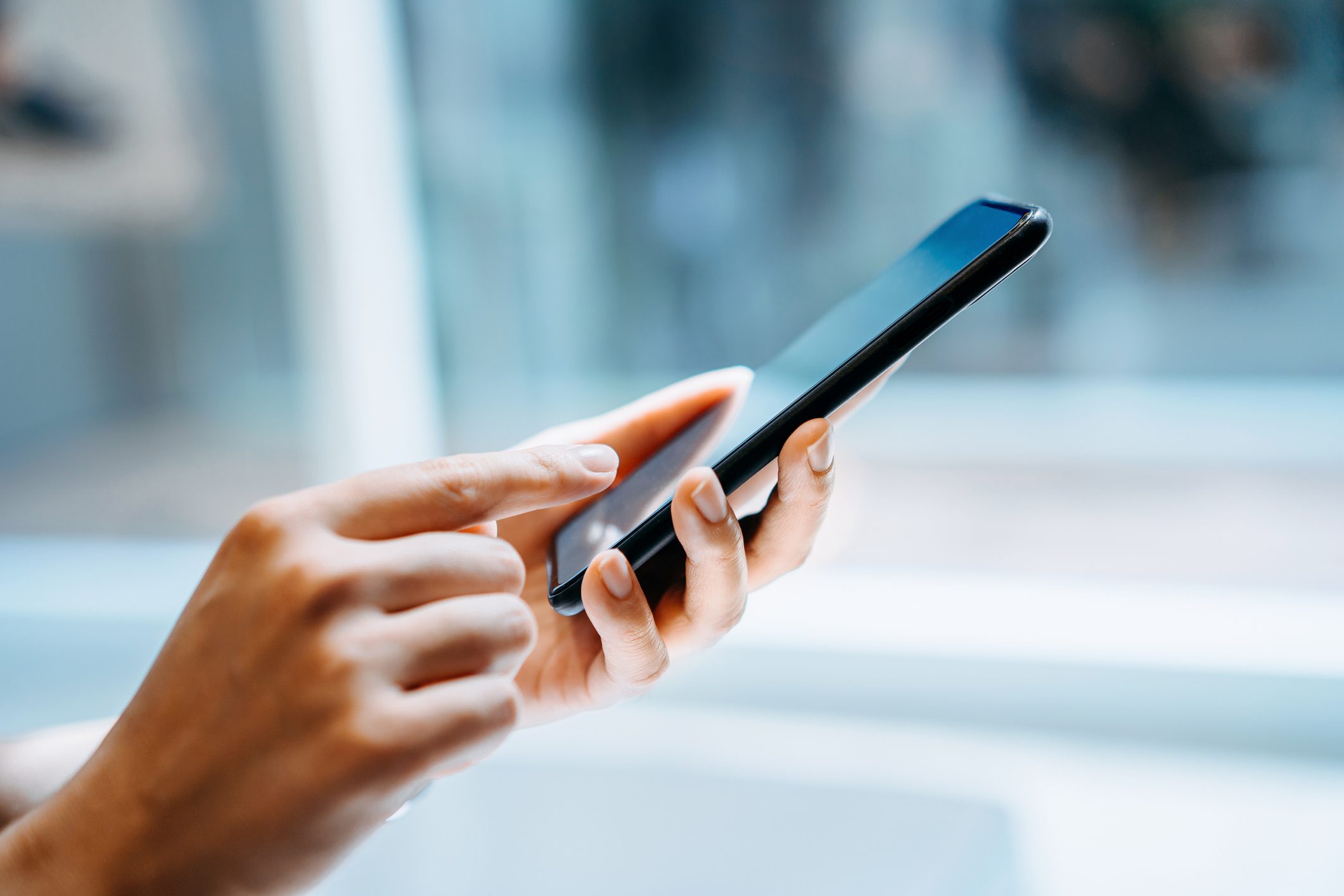 A person uses a smartphone with both hands, tapping the screen in a well-lit indoor setting.