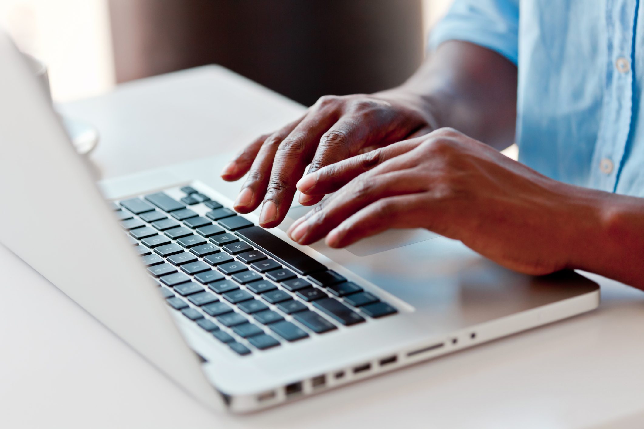 Hands typing on a laptop keyboard, situated on a white desk in a bright setting.