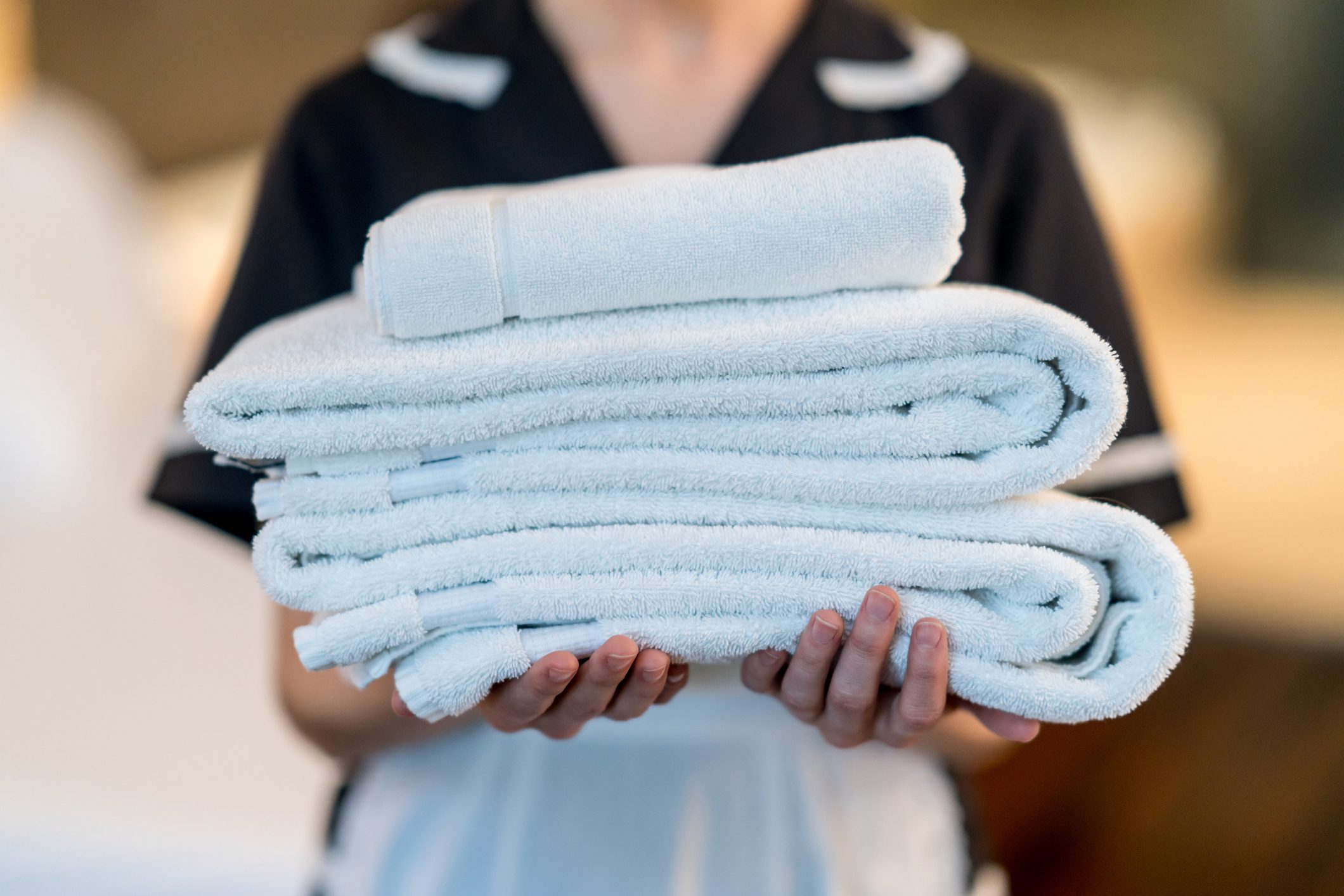 A person holds a stack of neatly folded white towels, wearing a uniform, indoors.
