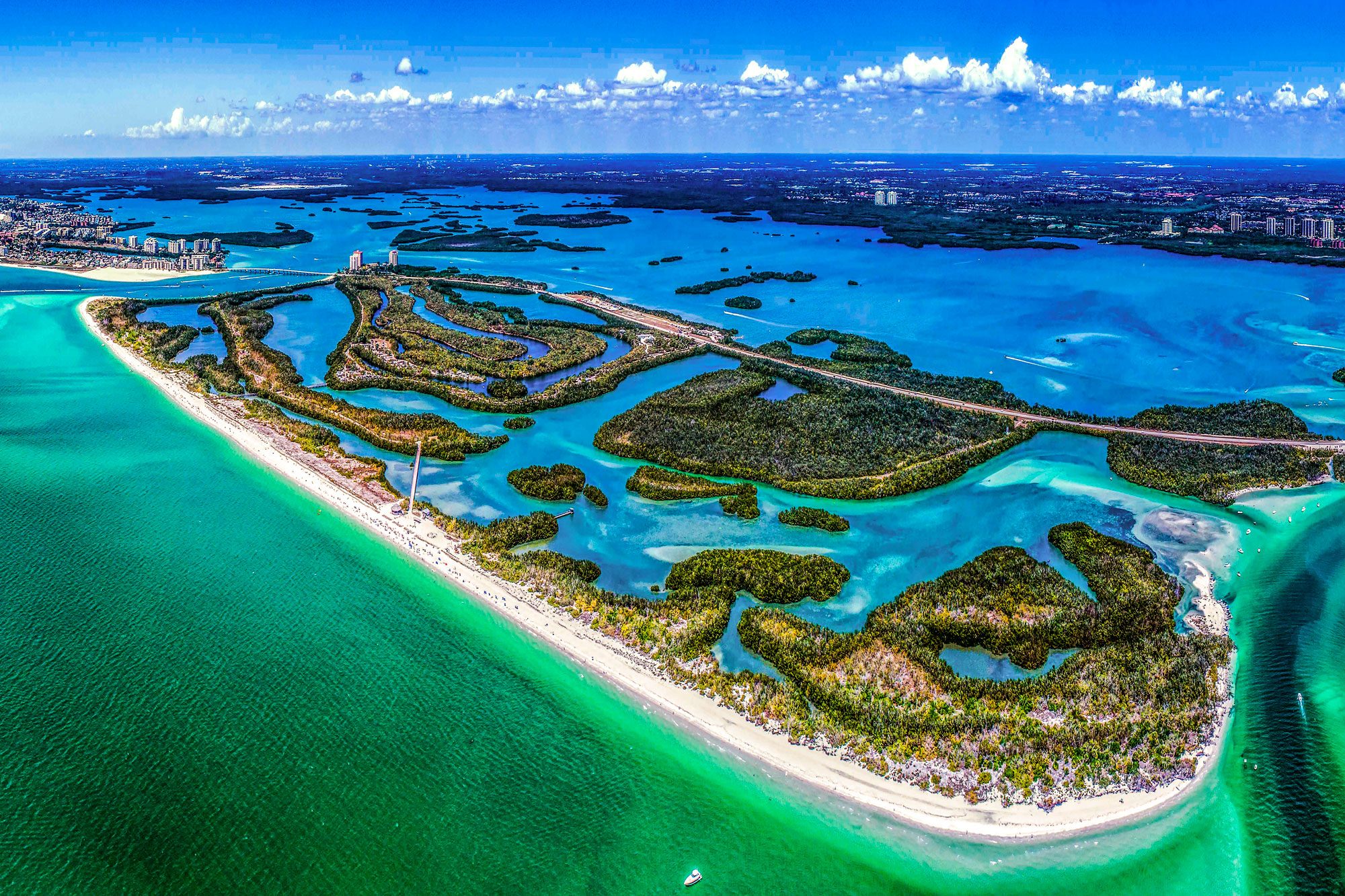 Aerial view of islands with lush vegetation, surrounded by vibrant turquoise waters, and a sandy beach stretches alongside a coastal cityscape.
