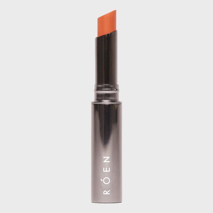 Lipstick extends from metallic tube, displaying orange color; text 