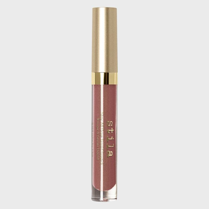 A tube of Stila liquid lipstick stands upright against a plain background, featuring a gold cap and translucent container displaying pinkish-brown color.