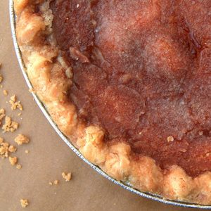 Pie resting on brown surface; golden crust surrounds warm, textured filling, with a few crumbs scattered nearby.