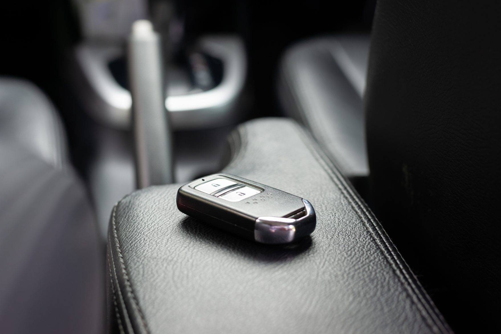 A car key remote rests on a leather armrest inside a vehicle, featuring buttons for lock and unlock functions.