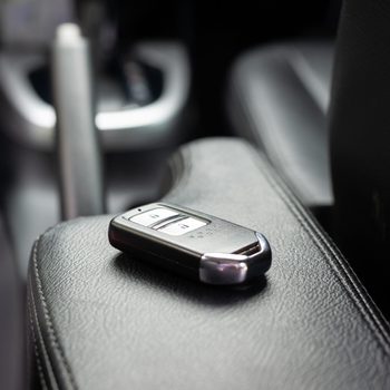 A car key remote rests on a leather armrest inside a vehicle, featuring buttons for lock and unlock functions.