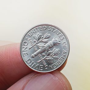 A dime held between fingers, featuring a torch with branches. Text reads 