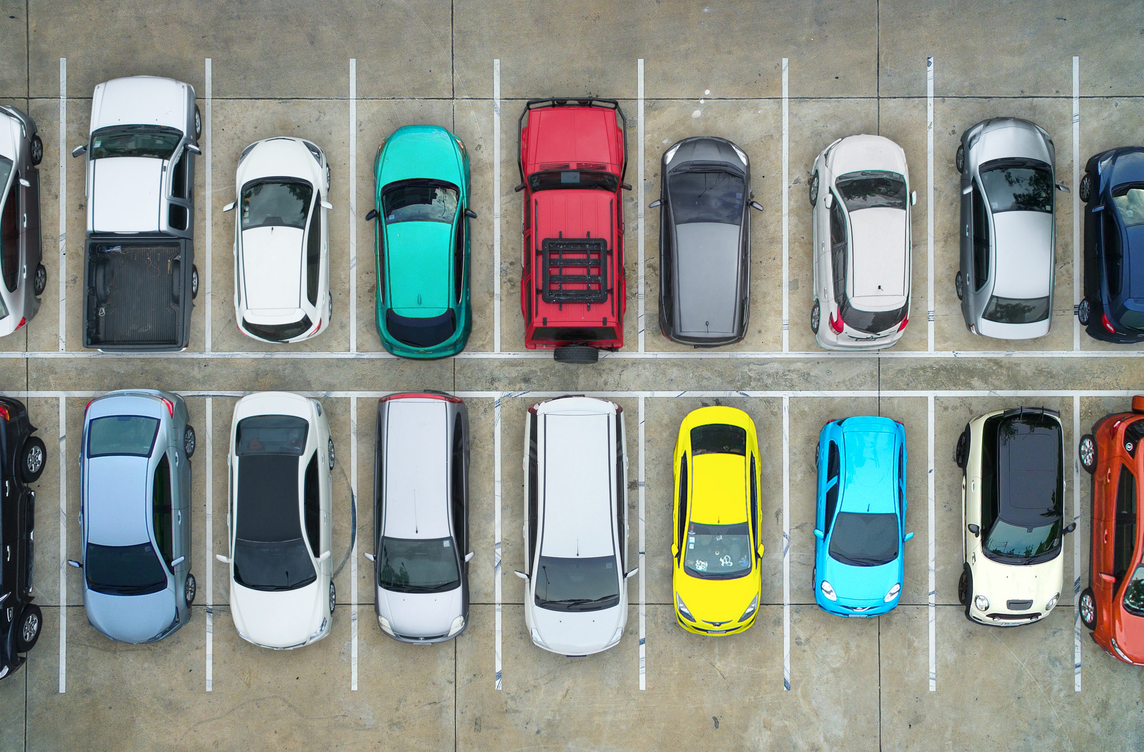 Vehicles parked neatly in two rows on a concrete lot, featuring a variety of colors including red, yellow, turquoise, and white.