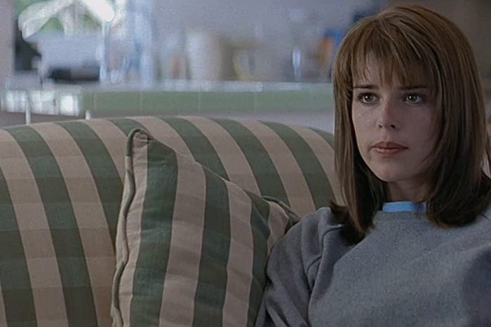 Woman sits on a striped sofa, looking thoughtful in a bright, softly focused room.