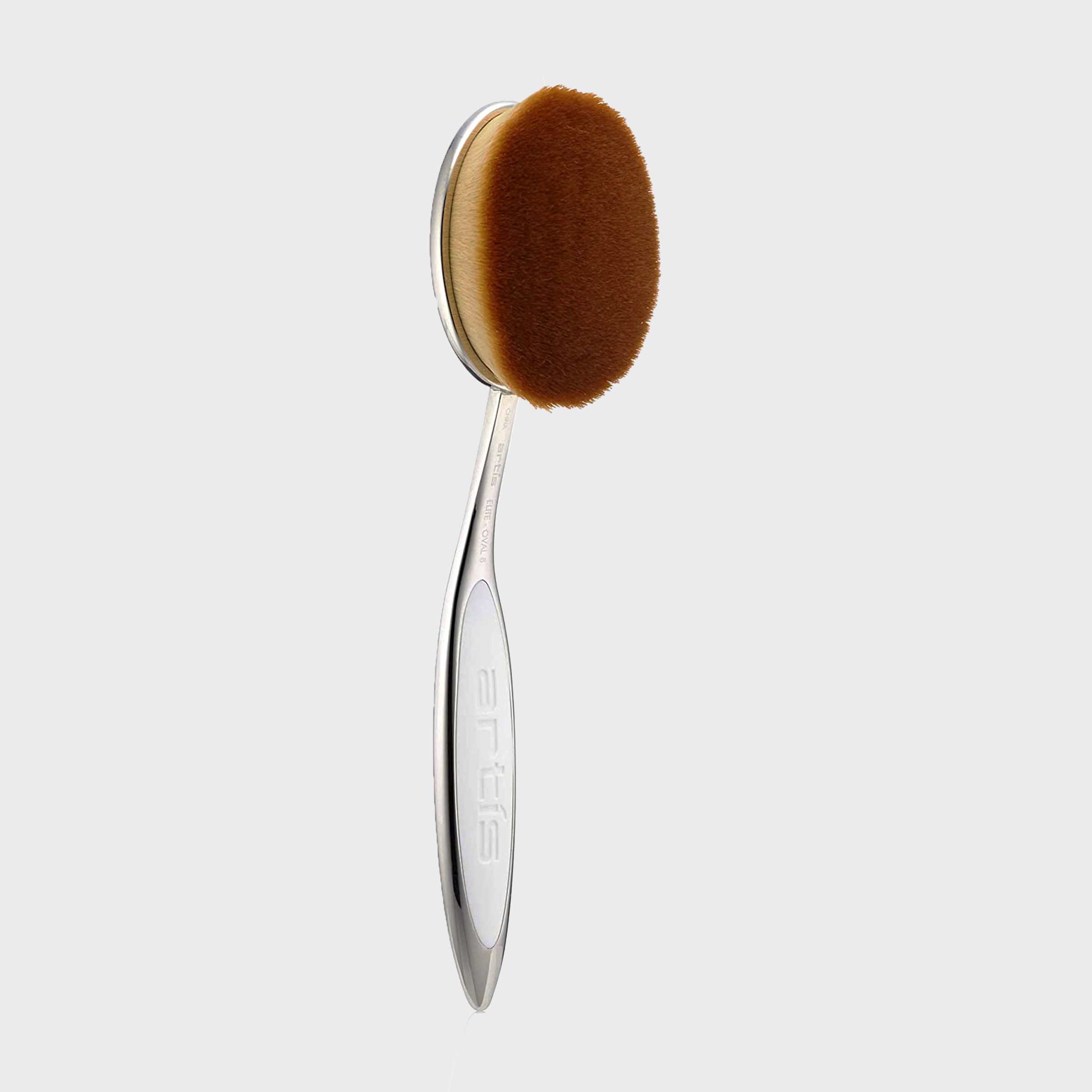 Oval makeup brush stands upright; sleek metallic handle with "artis" engraved, displayed against a plain white background.