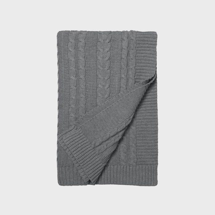 Gray, folded knitted blanket, featuring a cable pattern, lies flat on a plain white background.