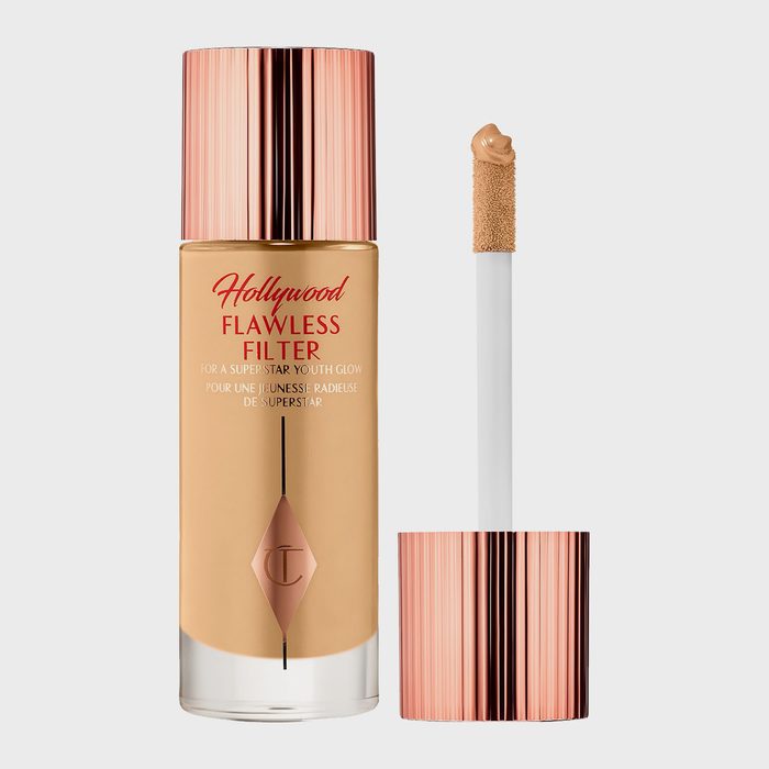 Foundation bottle standing with an open applicator beside it, featuring copper accents, against a plain background. Text reads: 