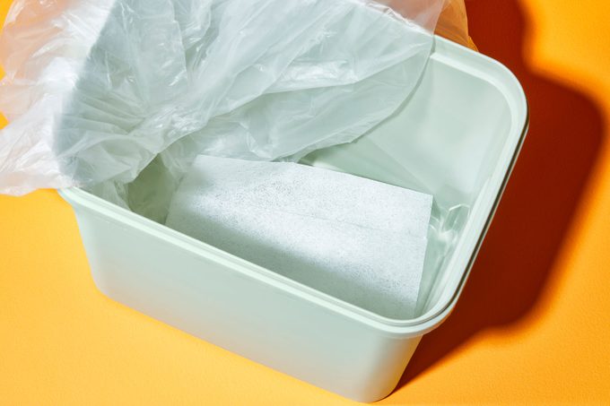 a dryer sheet at the bottom of a trash can with the bag pulled to one side so the dryer sheet can be visible; orange background