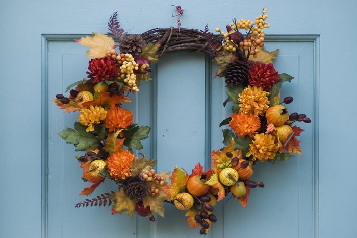 Wreath adorned with autumn leaves, pinecones, berries, and flowers, hanging on a blue wooden door.