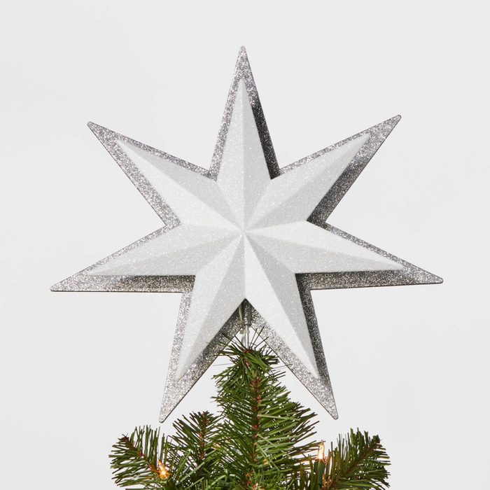 A glittery silver star sits atop a green Christmas tree against a plain white background.
