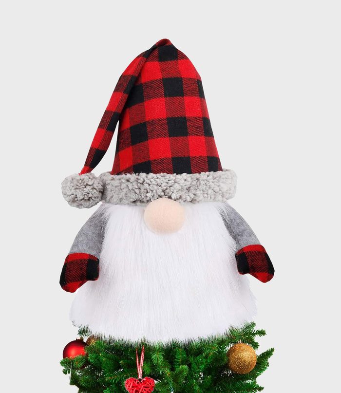 Gnome with a red plaid hat sits atop a decorated Christmas tree, against a plain background.