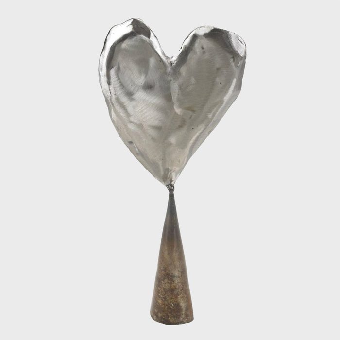 Metal heart atop a conical base stands upright on a plain, light gray background.