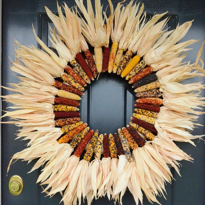 A wreath made of colorful corn cobs hangs on a dark-colored door.