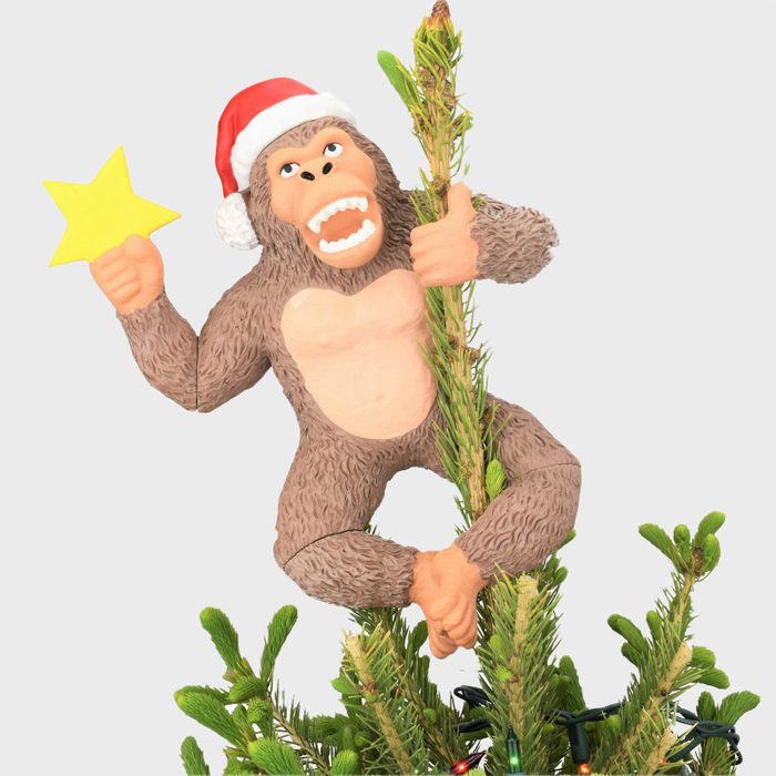 A gorilla wearing a Santa hat holds a yellow star, climbing a Christmas tree adorned with lights.