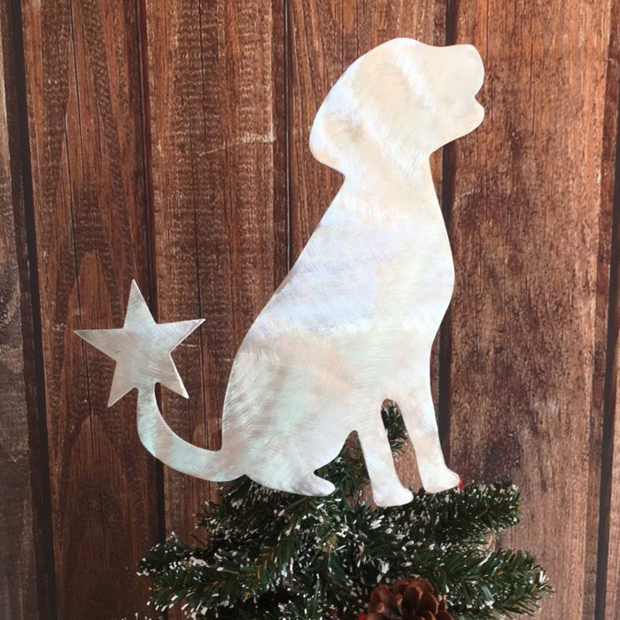 Metal dog silhouette with star tail tops a Christmas tree against a wooden backdrop.