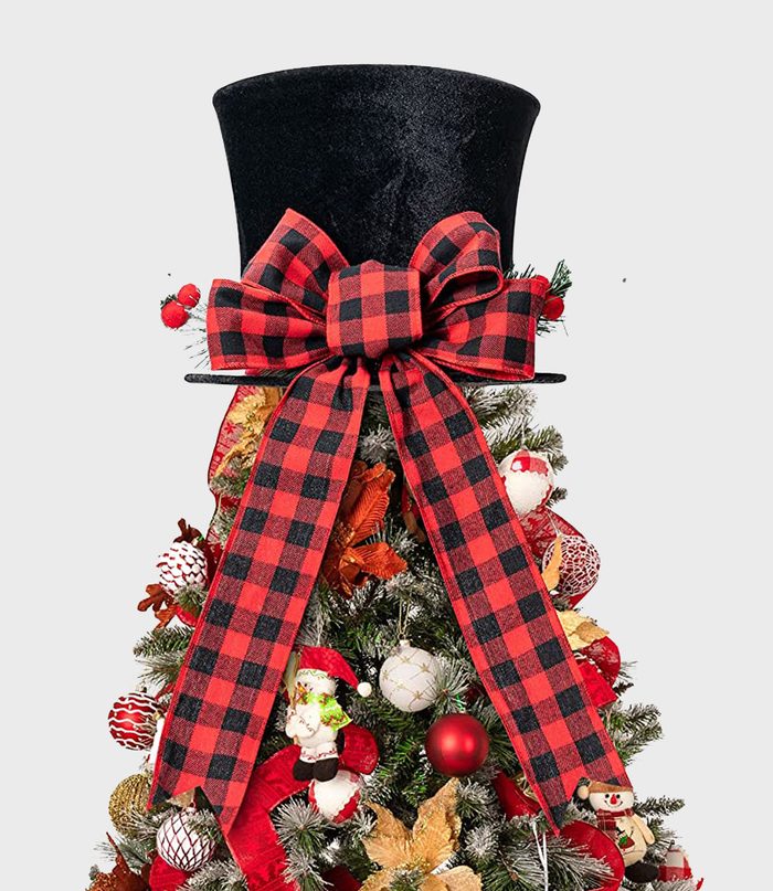 Top hat with red plaid bow resting atop a decorated Christmas tree, featuring red and gold ornaments amidst green branches.