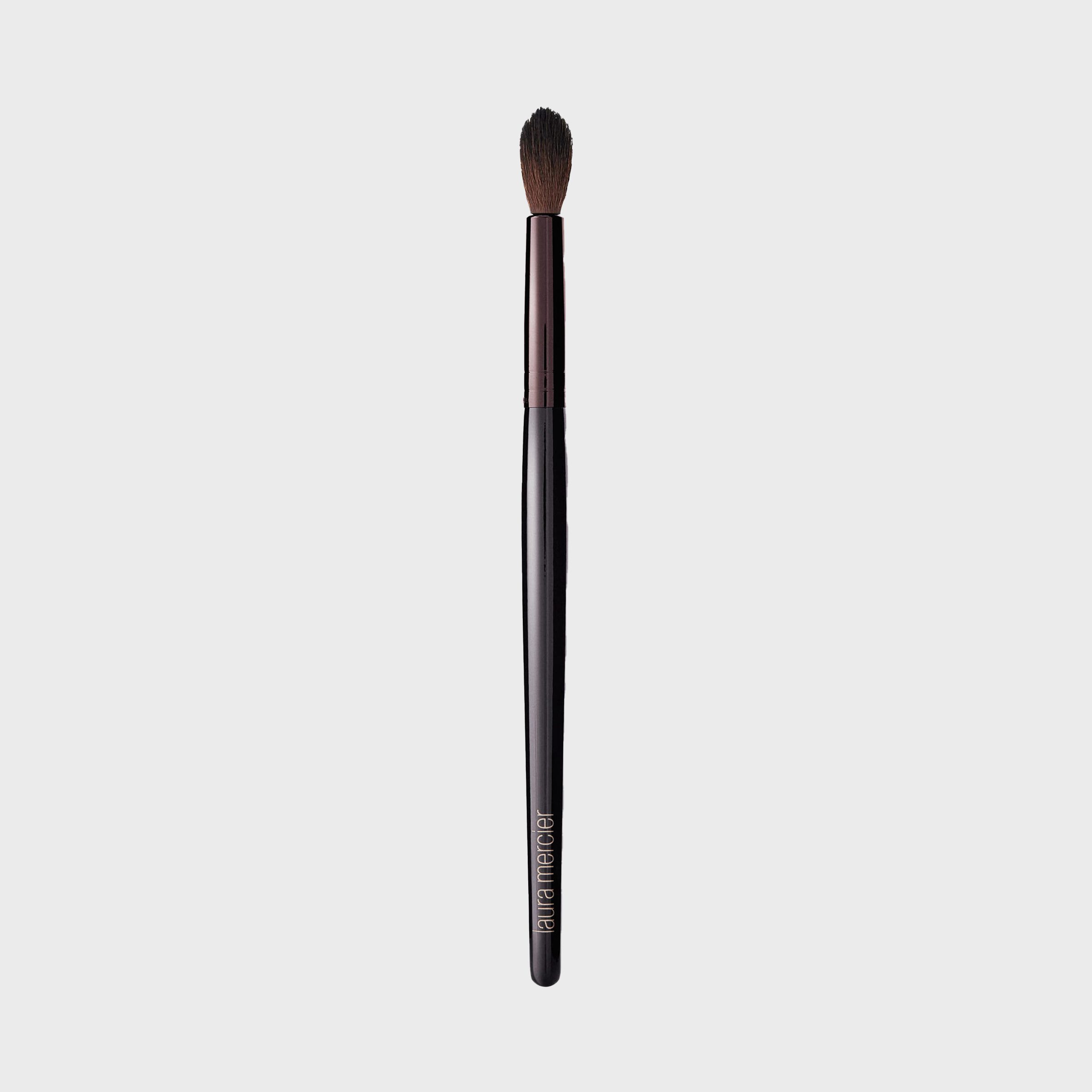 A makeup brush with a tapered tip displayed against a plain background. "Laura Mercier" is printed on the handle.