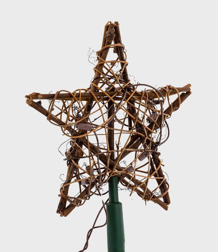 Star-shaped wooden ornament wrapped with thin vines, supported by a green stand, displayed against a plain background.