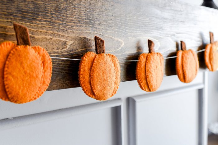Felt pumpkins hanging from a string on a wooden surface, creating an autumn-themed decoration above a gray paneled wall.