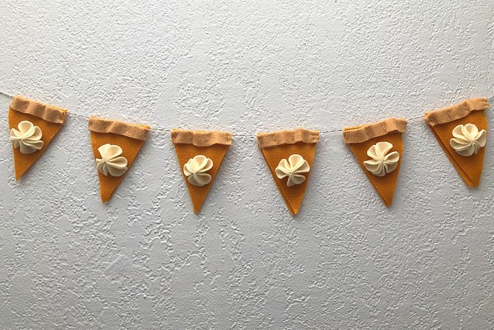 Fabric pie slice garland hangs, adorned with cream-like toppings, against a textured white wall.