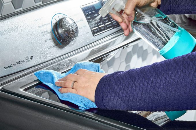 hands cleaning the exterior of a washing machine in a laundry room
