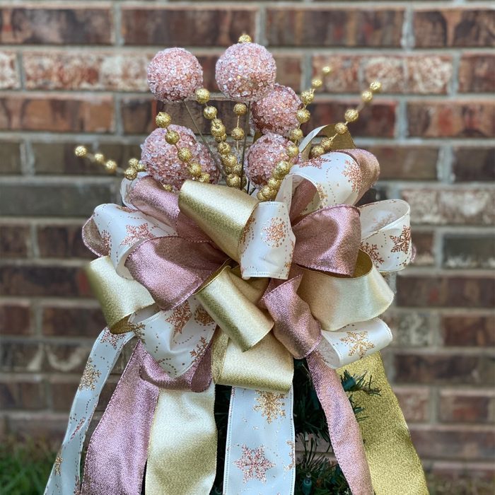 Decorative bow features shimmering ribbons and glittery pink spheres; displayed against a textured brick wall.