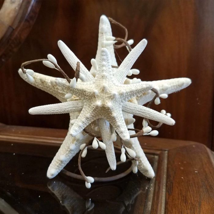 Starfish sculpture resting on a dark wooden surface, adorned with white decorative beads on thin branches, against a textured wooden background.