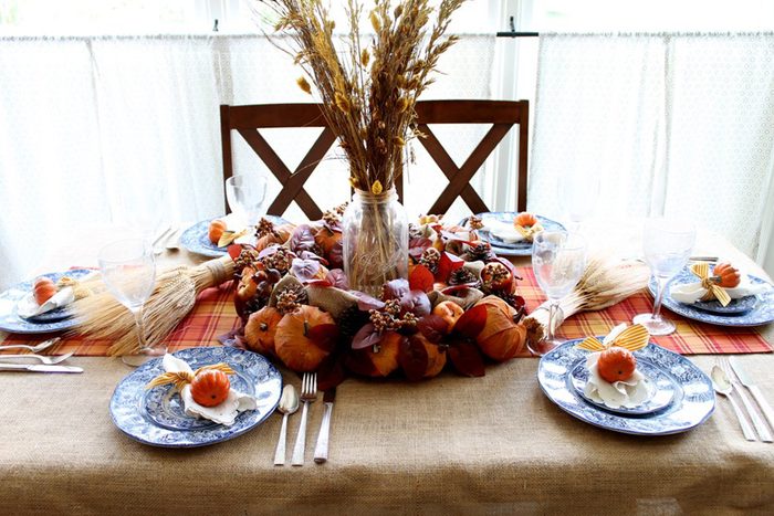 Table displays autumn centerpiece with pumpkins and leaves, surrounded by blue plates with mini pumpkins, in a bright dining room.