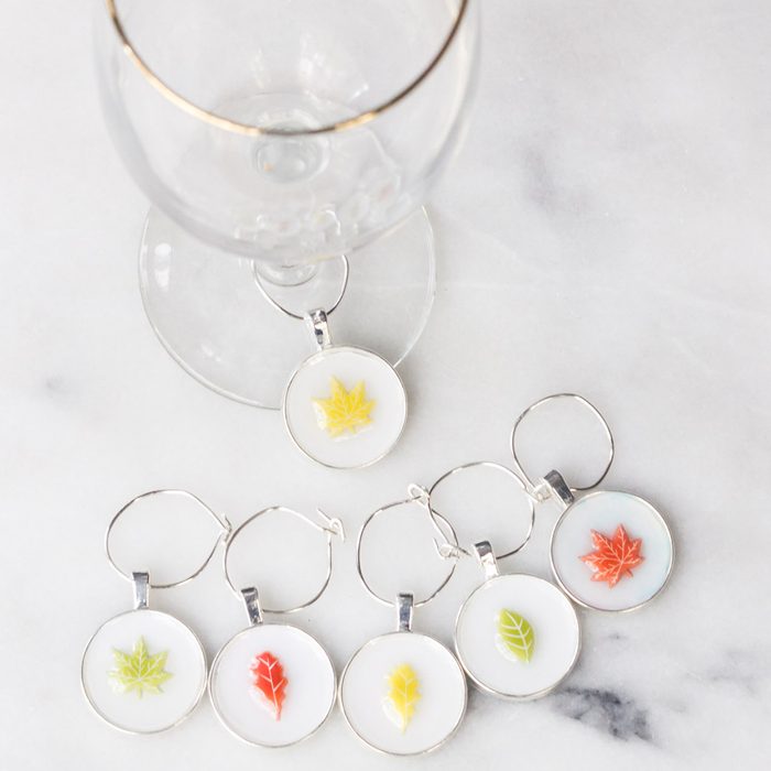 Wine glass with leaf charm attached; additional colorful leaf charms laid on a marble surface.